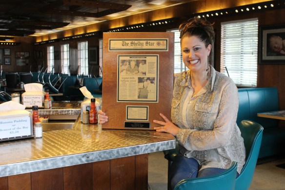 (The Star/Jessica Pickens) Natalie Ramsey, VP of Red Bridges Barbecue, remembers when Mickey Rooney visited the restaurant in 1997. She holds a Shelby Star article that hangs in the restaurant. 